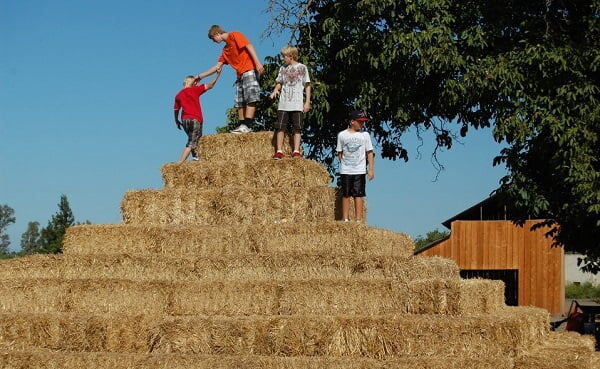 Kids helping each other climb the hand-stacked hay pyramid